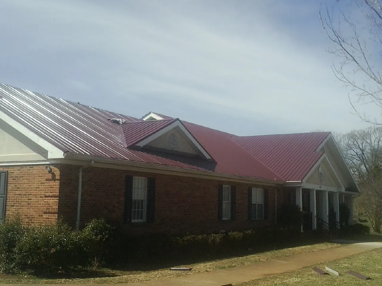Red metal roof with gabled entries on a long brick building, from a Hail Damage Roof Repair job in Duanesburg
