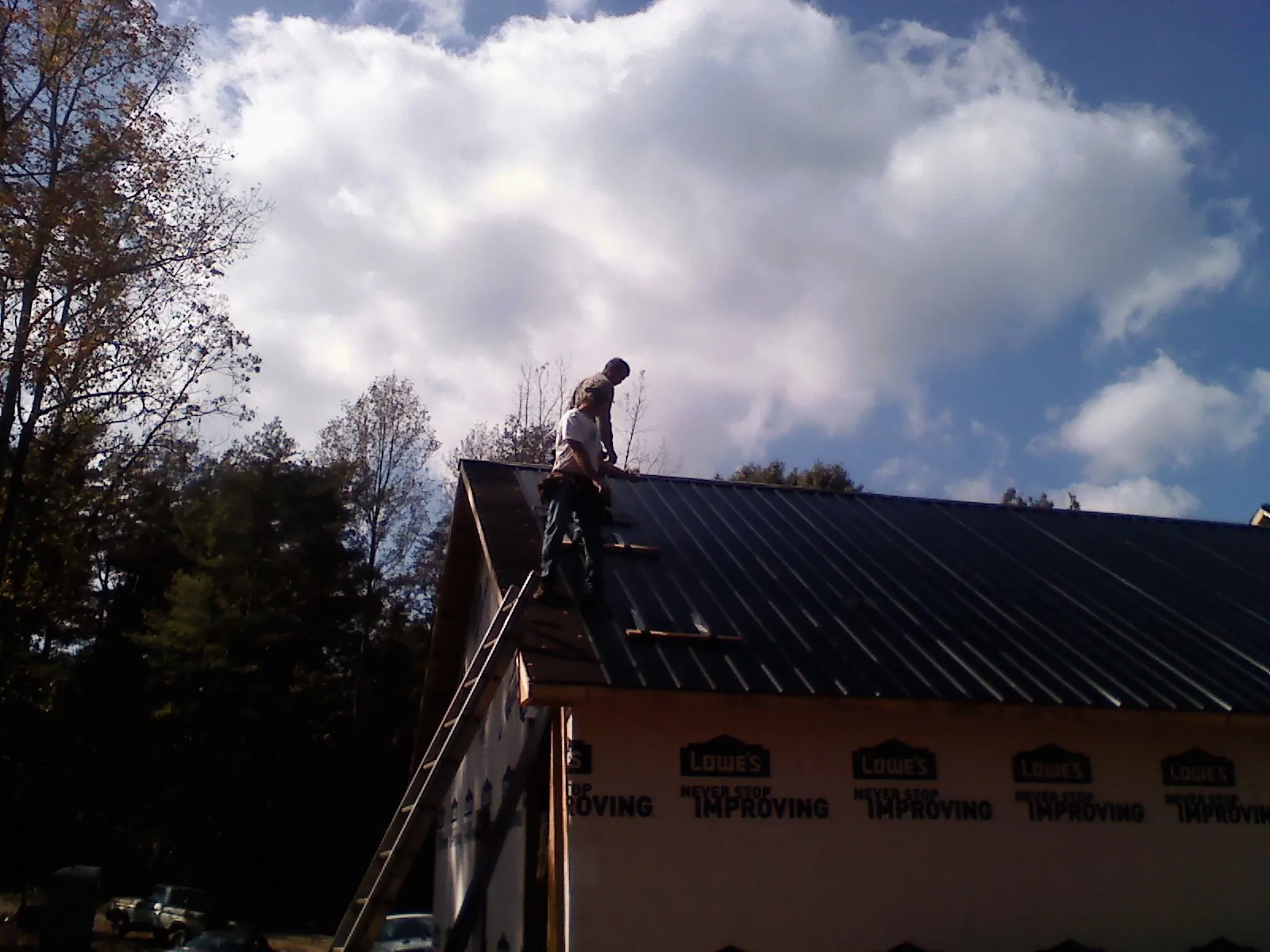 Roofer fastening dark metal panels high against a cloudy sky, from a Roof Inspection job in Duanesburg