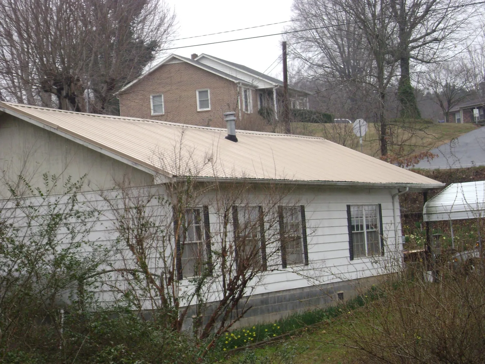 Tan metal roof on a white sided house set into a hillside — Commercial Roofing by Roofing Brothers in Duanesburg