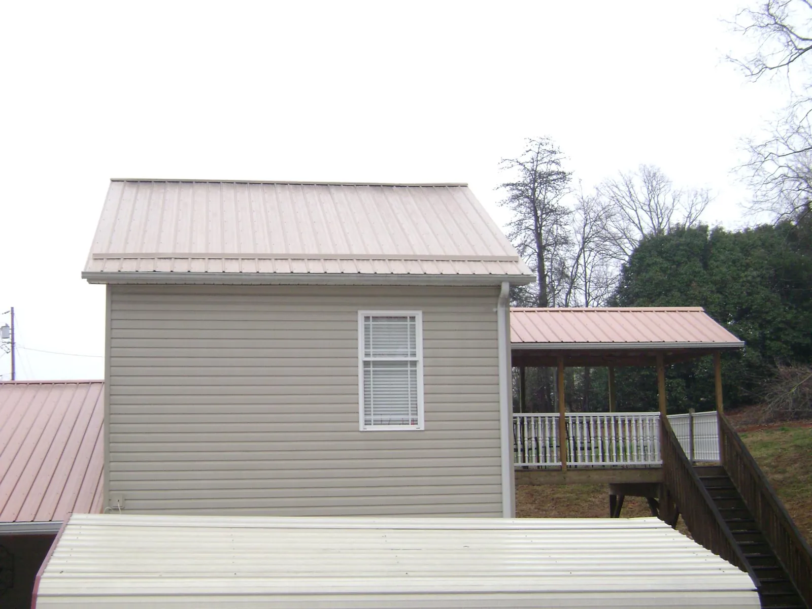 Tan metal roofs on a two story addition and attached porch, from a Roof Replacement job in Duanesburg